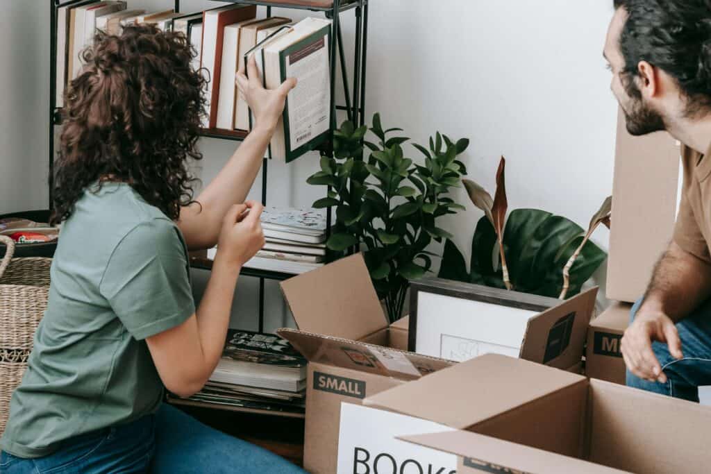 A couple is placing books on the shelves as they are unpacking boxes.